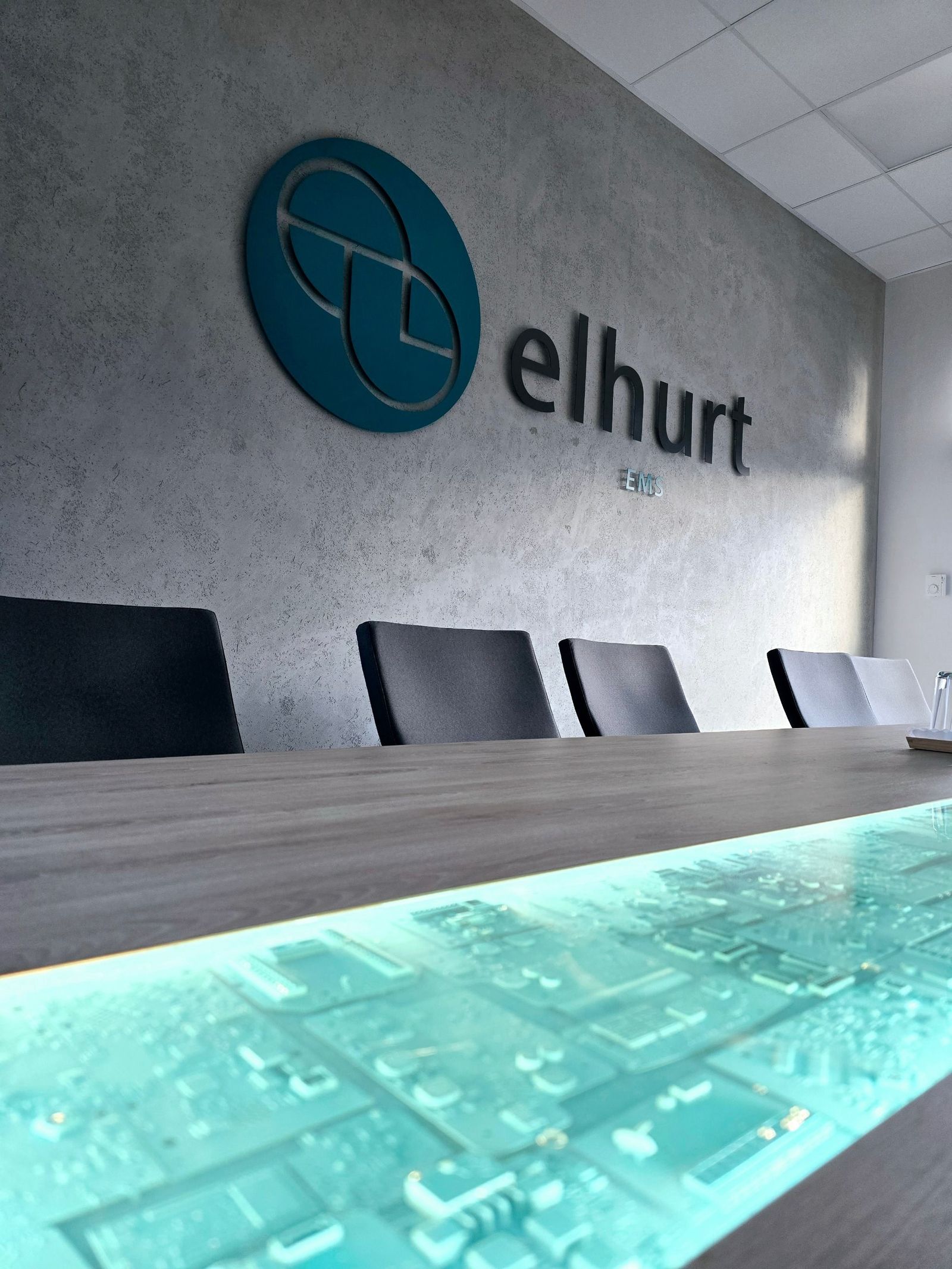 Sala konferencyjna: logo elhurt EMS na ścianie z betonu architektonicznego, stół z podświetlonym pasem z płytek drukowanych