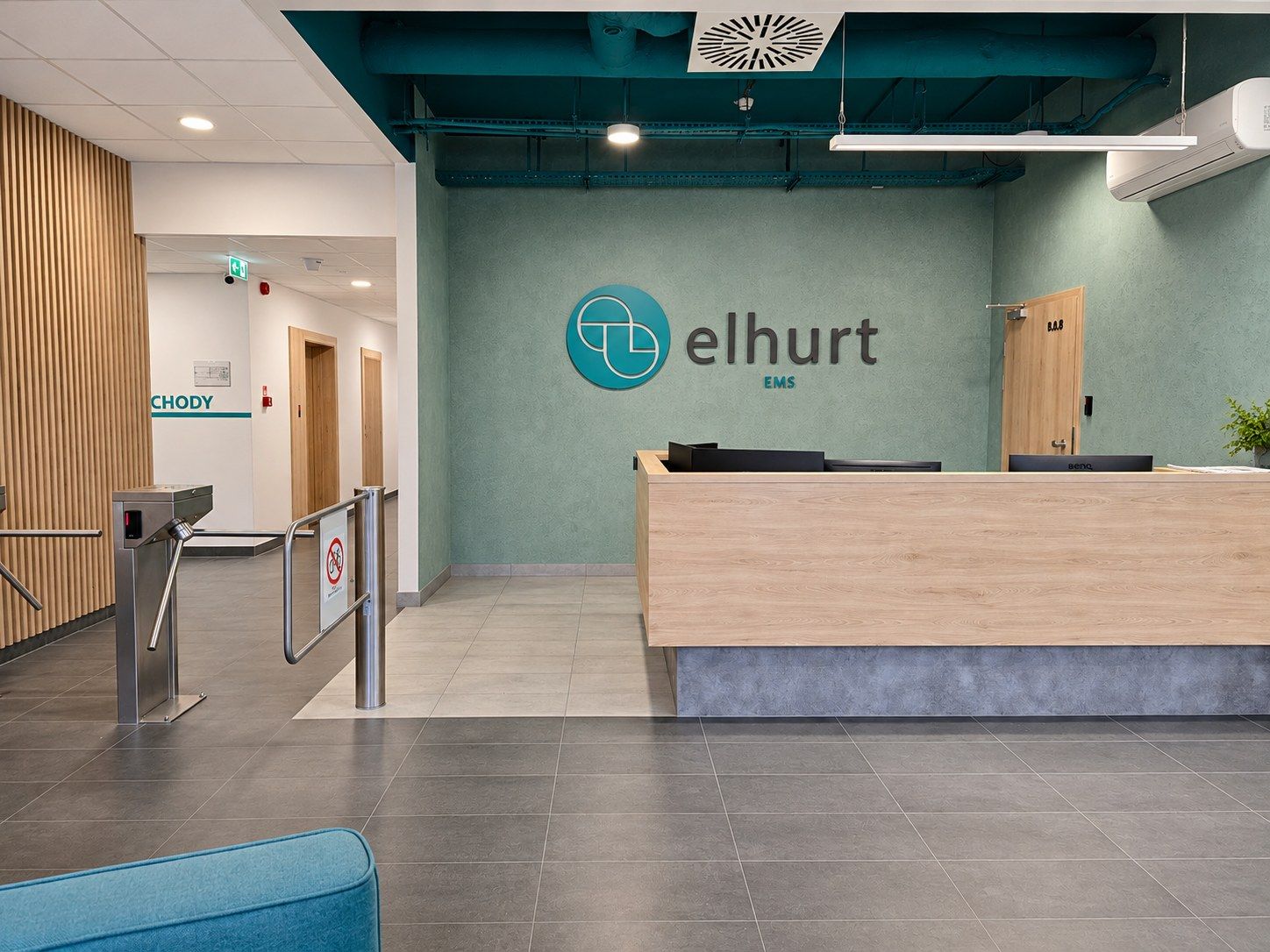 Recepcja z drewnianą ladą, turkusową ścianą i logo elhurt EMS